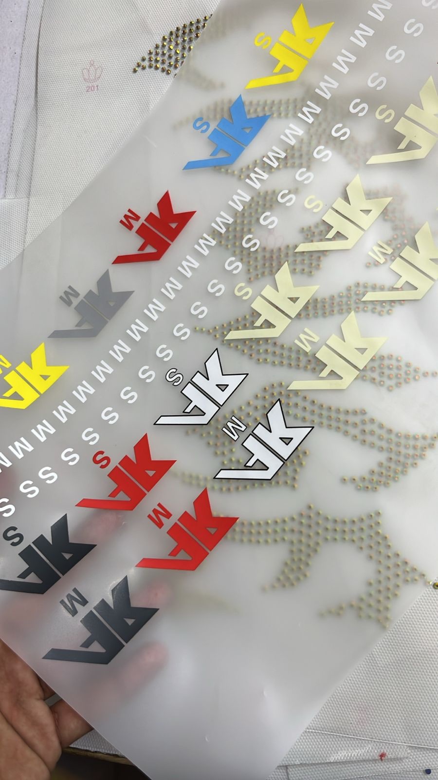 Hand-set rhinestone letter patches and woven CRSVGE neck labels laid out on a dark surface